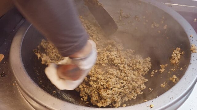 Close up view of chef using two spatulas mixing buckwheat crispy with boiling malt sugar in iron pan, 4k slow motion footage, Chinese traditional food concept.