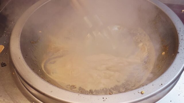Close up view of chef using two spatulas mixing buckwheat crispy with boiling malt sugar in iron pan, 4k slow motion footage, Chinese traditional food concept.