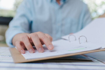 Businessman hand reviewing financial report on paper document in binder, analyzing data and planning business strategy in office environment Focused workplace concept.
