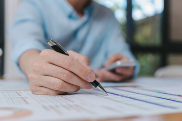 Close-up of businessman holding smartphone and writing on paper document, multitasking during data review or financial analysis in office workspace Modern business communication concept.