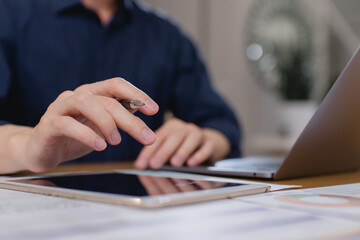 businessman working with tablet and laptop, holding pen and analyzing digital data and financial charts in modern office environment. Digital transformation in business concept.