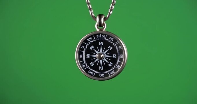 A silver compass pendant hangs from a chain against a green screen background