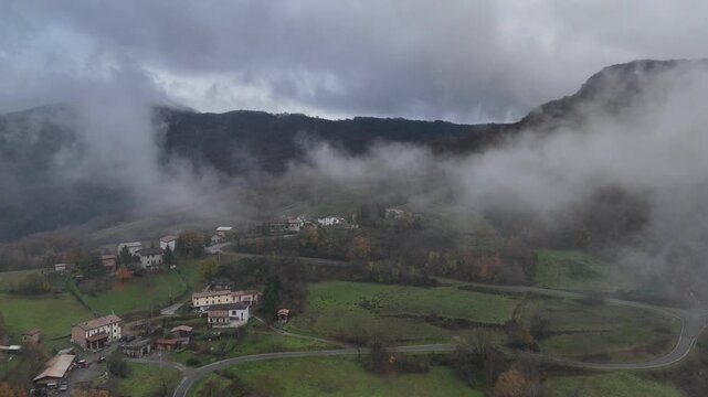 Fog rolling over forested hills and a small green field in Castelletto Val Tolla, Emilia Romagna, painting a mysterious and tranquil winter scene with a thick blanket of haze