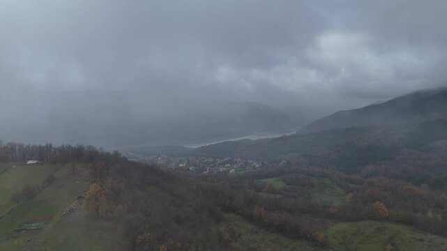 Fog rolling over forested hills and a small green field in Castelletto Val Tolla, Emilia Romagna, painting a mysterious and tranquil winter scene with a thick blanket of haze