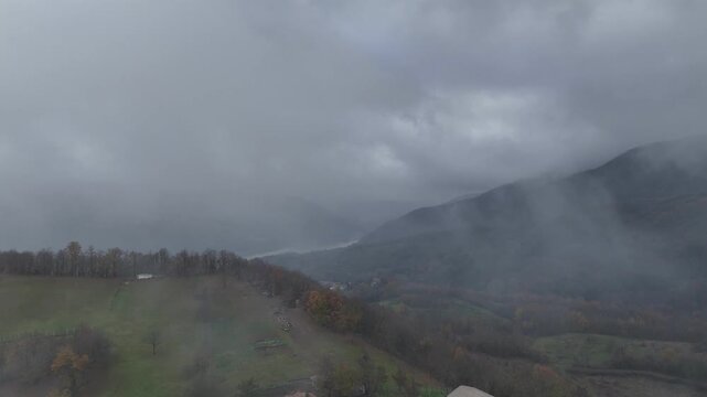 Fog rolling over forested hills and a small green field in Castelletto Val Tolla, Emilia Romagna, painting a mysterious and tranquil winter scene with a thick blanket of haze