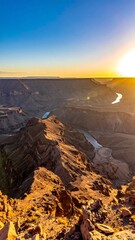 High angle view of canyon landscape with river winding through, bathed in the warm glow of the setting sun