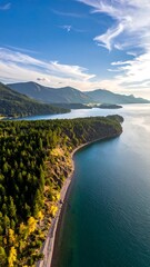 Coastal mountains landscape with trees, clear blue water, and a partly cloudy sky under bright sunlight