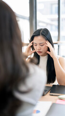 Stressed Asian businesswoman feeling tired or having a headache during a difficult office meeting.
