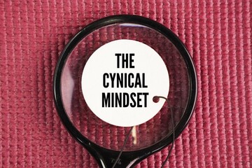 A magnifying glass and a paper tag with the words the cynical mindset. an attitude of distrust towards claimed ethical and social values ​​and a rejection of the need to be socially involved
