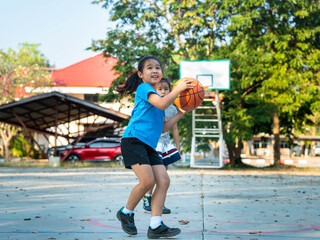 Two young girls playing basketball together on outdoor court