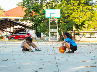 Two young girls resting with basketball on outdoor court