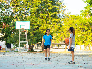 Two young girls playing basketball together on outdoor court
