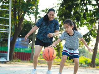 Mother and daughter played basketball together on an outdoor court during sunset.