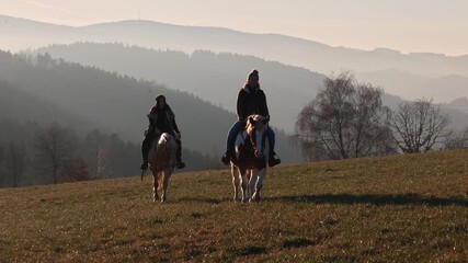 Two women riding horses toward the camera at golden sunset, friendship, companionship and shared equestrian lifestyle