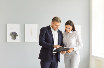 Portrait of young confident man professional realtor standing with female client in modern new apartment discussing contract buying property. Move, rent and real estate market concept.