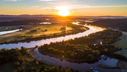 Aerial view of a wide river snaking through a green landscape. The sun bathes everything in a warm, golden light at sunrise
