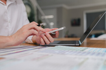 Close-up of a businessman using a smartphone and laptop at a desk with financial documents. Concept of online banking, financial analysis, remote work, and business technology