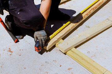 Worker is measuring wooden beams boards with tape measure on construction site