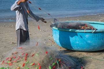 Fisherman casting net from beach beside blue boat with colorful floats and ocean backdrop
