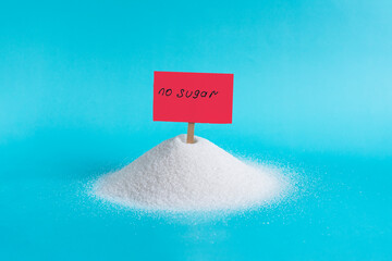 A large mountain of granulated sugar and a bright red sign stuck in it with the inscription "no sugar" in close-up on a light background