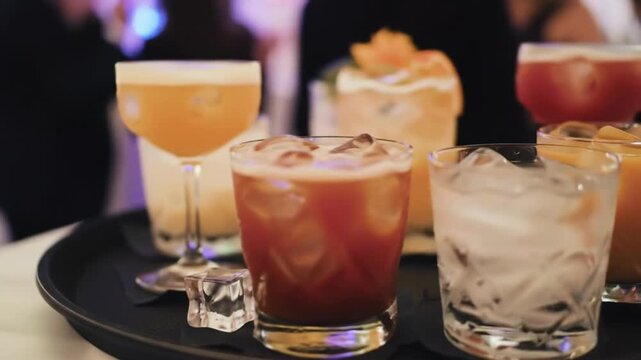 A selection of five glasses containing colorful drinks with ice and garnishes on a black tray