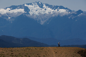 A man walks along a path, with huge mountains visible in the background.