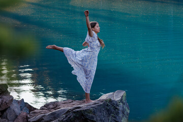 A girl is dancing on the shore of a blue lake.