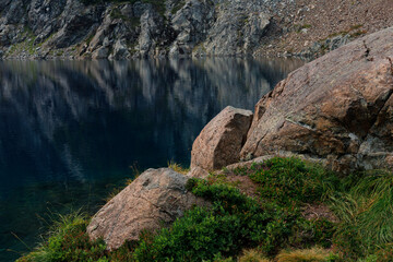 Obraz premium Rocks covered with grass are located on the shore of a mountain lake.
