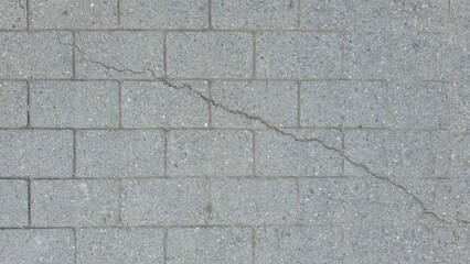Cracked gray concrete paving stone texture background. A prominent diagonal crack on this sidewalk or walkway surface indicates damage or decay. The old gray concrete floor tiles have cracks.