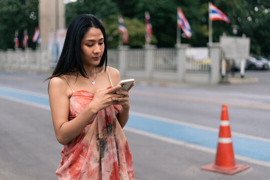 Young woman texting on smartphone by road with thai flags and traffic cone