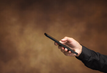 Hand holding smartphone with copy space on brown background.