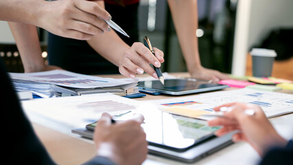 Close-up of business people hands pointing at data charts and using a tablet during a strategy meeting in a bright, modern office space.