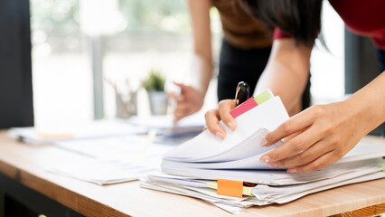 Close-up of business people hands working with documents, organizing paperwork, and analyzing files in office.