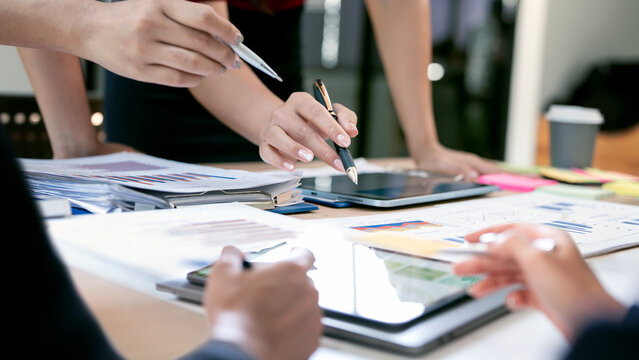 Close-up of business people hands pointing at data charts and using a tablet during a strategy meeting in a bright, modern office space. - Powered by Adobe
