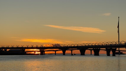 A beautiful sunset over a calm body of water with a bridge silhouetted against the sky