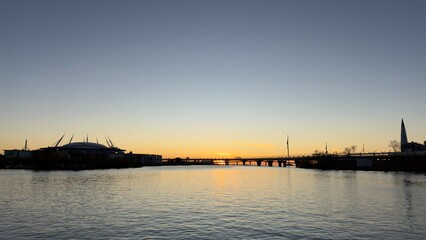 Fototapeta premium A serene sunset over a river, with silhouettes of buildings and a bridge in the foreground