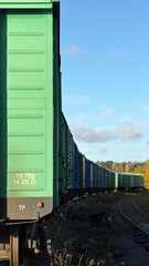A row of green freight train cars on a railway track under a blue sky