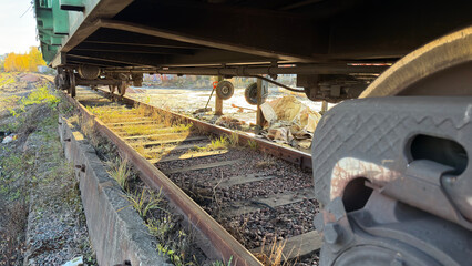 An abandoned railway track with overgrown grass and weeds, showing the undercarriage of a train car, highlighting neglect and decay