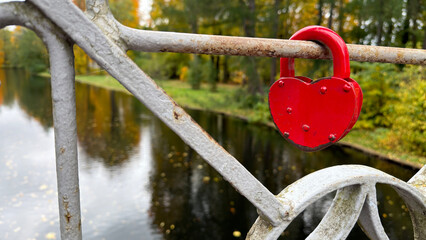 Red heart-shaped padlock on a bridge railing over a river.