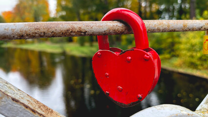 Red heart-shaped padlock on a metal railing by a river.