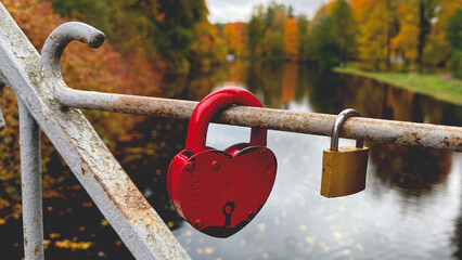 Heart-shaped red padlock on a bridge railing with autumn background.