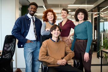 Diverse group of young adult men and women posing together in modern office, smiling and looking at camera, representing multiethnic business team collaboration and teamwork