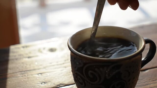 A dark-colored ceramic mug with a swirling pattern sits on a rustic wooden table, filled with dark liquid and a spoon