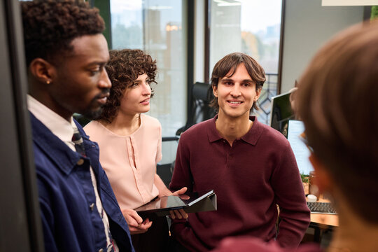 Group of young adult multiethnic colleagues discussing project in modern office, Caucasian woman holding digital tablet while Black man and Caucasian woman listening attentively