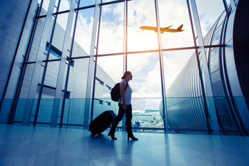 travel by flight, silhouette of passenger in airport, woman walking with luggage in airport, airplane flying in the sky on background