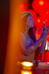 A tattooed woman uses her phone amidst vibrant red and purple lighting, creating a captivating scene filled with energy and intrigue.
