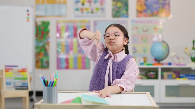 Unhappy Asian schoolgirl giving thumbs down in classroom