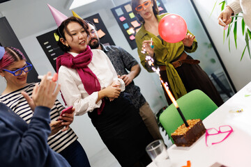 Business celebration with cake and festive atmosphere at a team event featuring employees wearing party hats