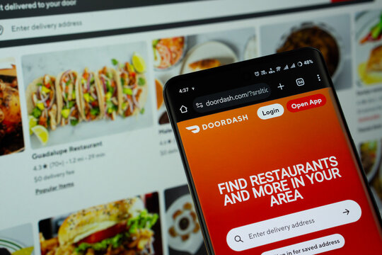 Dhaka, Bangladesh - 16 March 2025: The app of the DoorDash is displayed on a smartphone screen, and the website is visible on a computer screen in the background.