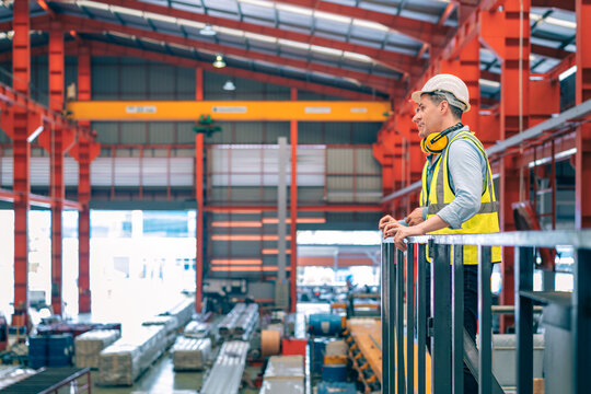 Caucasian industrial engineer men wear safety helmet vest standing on elevated catwalk supervising factory floor. Manager partner pointing future vision in manufacturing plant. Heavy metal industry